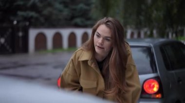 Trafik kazasında arabalara bağıran öfkeli, hoşnutsuz genç kadın. Kızgın Kafkasyalı tatminsiz kadının portresi yağmurlu bir günde dışarıda bağırıyor.