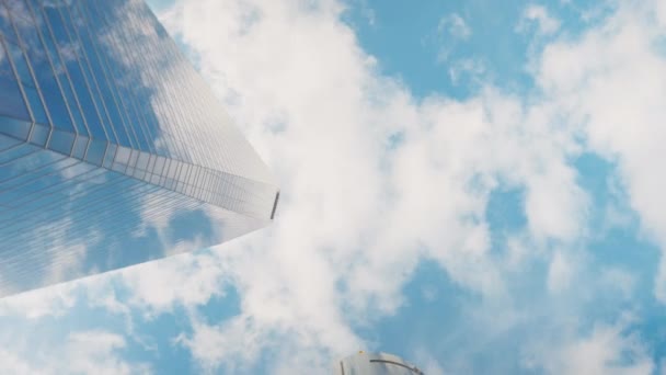 底部的角度观看城市摩天大楼与现场摄像头旋转 蓝天背景下的巨大玻璃商业建筑 户外白云密布 — 图库视频影像