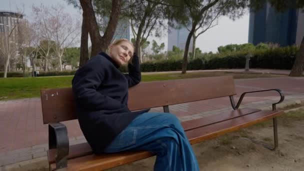 シティパークのベンチに座っている満足したリラックスした女性の周りにズームインしてパンニングライブカメラ 週末の朝のレジャーを楽しんでいるケアフリーの白人女性の肖像画 — ストック動画
