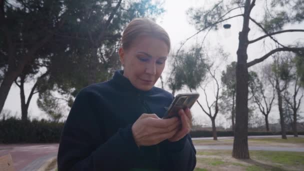 Şehir Parkındaki Bankta Oturan Akıllı Telefon Uygulamasında Internetten Mesajlaşan Sarışın — Stok video