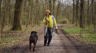Geniş açı pozitif genç kadın köpekle birlikte ormandan ayrılıyor. Kendine güvenen beyaz ev sahibi ve evcil hayvanın portresi açık havada parkta eğleniyor.