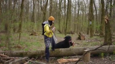 Beyaz, kendine güvenen, iri siyah köpekli genç bir kadın ormanda yürüyor. Güzel bir bayanın açık havada eğlenirken geniş açılı portresi.