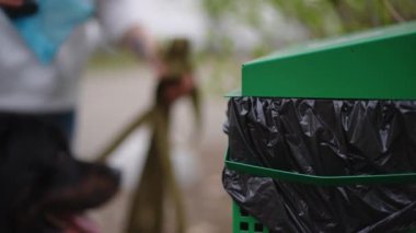 Parkta, tanınmayan bir kadının köpek kakasını attığı özel bir çöp kutusu var. Yakın plan beyaz kadın. Çöpü dışarı atıyormuş.