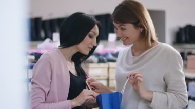 İçerideki ayakkabı dükkanında duran arkadaşına yeni ayakkabılarıyla böbürlenen tatmin olmuş bir kadın. Gülümseyen mutlu beyaz kadın Kara Cuma günü alışveriş çantasıyla gösteriş yapıyor.