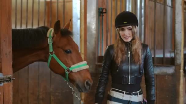 跟踪拍摄到一个自信的年轻貌美的女人带着一匹棕色的优雅的马走出马厩 现场摄像头跟随专业的高加索女骑手和宠物在谷仓里散步 — 图库视频影像