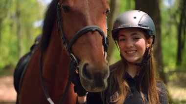 Saf atlarla poz veren kahverengi gözlü zayıf esmer kadının portresi. Mutlu, kendine güvenen, dişlek gülüşlü beyaz atlı, güneşli ormandaki hayvanları okşayan kameraya bakıyor.