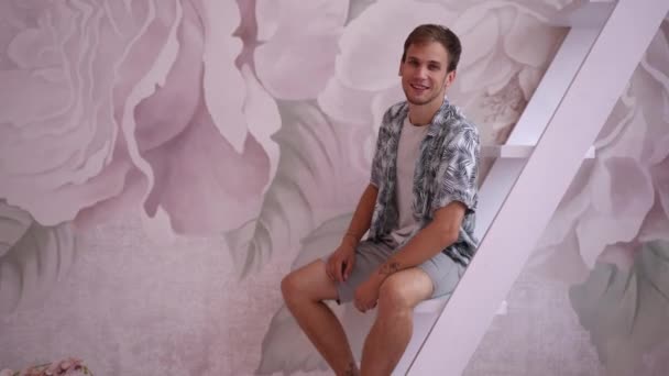 Joven Hombre Confiado Sonriendo Sentado Las Escaleras Dentro Mirando Cámara — Vídeos de Stock
