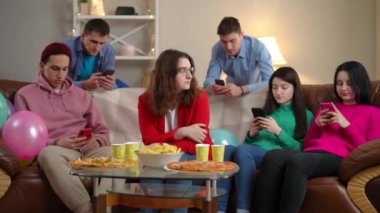 Üzgün, genç bir kadın kanepede oturmuş, telefon uygulamalarını kaydıran arkadaşlarına bakıyor. Kafkasyalı kadının portresi internet bağımlılığı tarafından özümsenmiş erkek ve kadınlarla parti yapıyor.