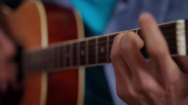 Yakın çekim erkek elleri gitar fretboard ve telleri çalıyor. Yakından tanınmayan genç, beyaz, yetenekli bir adam içeride hobi ediniyor.