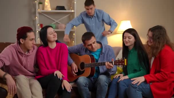 Joven Talentoso Tocando Guitarra Para Grupo Amigos Felices Sentados Sofá — Vídeos de Stock