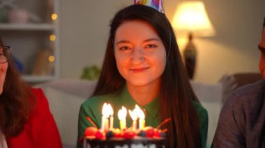 Kendinden emin gülümseyen genç bir kadının ön manzara portresi elinde mumlarla pastaya bakan arkadaşları tebrik ediyor. Kafkasyalı mutlu bayan tatilini evde kutluyor.