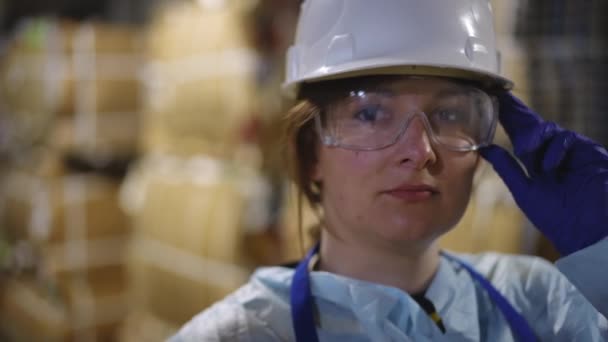 保護眼鏡とリサイクルステーションのハードハットで自信を持った白人女性のヘッドショットの肖像画 屋内で立っているカメラを見ているクローズアップ笑顔労働者 — ストック動画