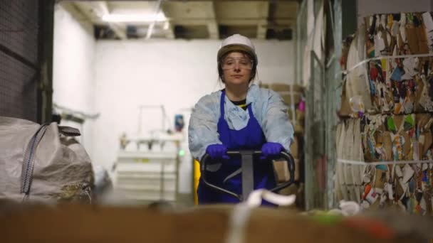 フロントビューは プッシュカートにパックされたゴミを押し出し 去る女性を集中させました 屋内のリサイクルステーションでゴミを移動する集中的なコーカサス人の従業員の肖像画 — ストック動画