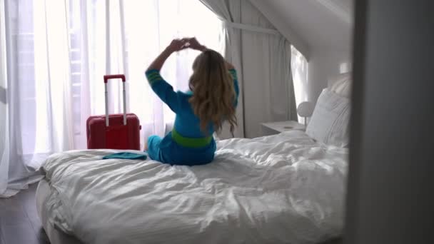 バックビューは ライブカメラズームとしてベッドに落ちるスチュワーデスのユニフォームでリラックスした幸せな女性 館内ホテルの客室でのレジャーを楽しむフライトアテンダント — ストック動画