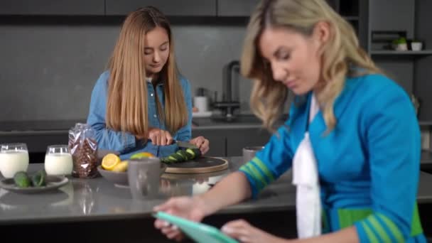 Concentrated Teen Daughter Cutting Vegetable Salad Blurred Mother Stewardess Scrolling — Stock Video