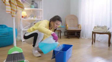 Genç bir kadın çamaşır deterjanını sepete suyla dolduruyor. Evdeki oturma odasında kendine güvenen beyaz ev kadınlarının geniş açılı portresi.