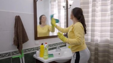 Yan bakış ciddi genç bayan evin içinde banyoda ayna temizliyor. Yoğunlaştırılmış Kafkas ev hanımı servisi profesyonel olarak çalışıyor. Bardakları kumaş ve deterjanla ovuyor.