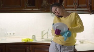 Kadın portresi telefonda konuşuyor bulaşıkları yıkıyor yemek takımlarını havluyla kurutuyor. Evdeki mutfakta beyaz bir ev hanımı var.