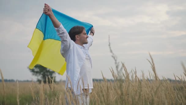 ウクライナの旗を持つ笑顔のハンサムな男の横の角度の肖像画は 小麦畑に立って離れて見ている手を伸ばしました 中型ショットコーカサス信頼できる男 屋外で一日中楽しむ — ストック動画