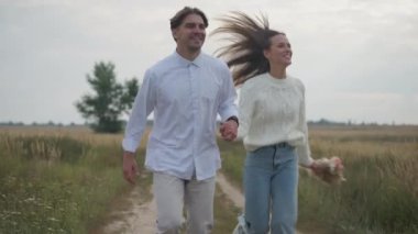 Dolly, el ele tutuşup ağır çekimde ayrılan mutlu çifti vurdu. Gülümseyen beyaz erkek ve kadın güler yüzlü, dışarıda sonbahar sahasında eğlenerek eğlenirler.