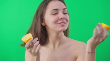 Önden bakan neşeli genç kadın, limon dilimlerini gözlerine yerleştiriyor ve gülümseyen kameraya bakıyor. Neşeli, gevşemiş Kafkasyalı kadın. Sağlıklı vitaminli organik meyve ve kromakey arka planda poz veriyor.