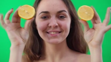 Neşeli genç bir kadının portresi limon diliyle gözlerini kapatan kameraya bakıyor. Ön cephede neşe saçan beyaz kadın yeşil ekranda meyvelerle poz verirken eğleniyor.