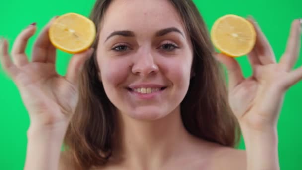 照片的正面是一个快乐的年轻女子 她看着镜头 用柠檬的一半遮住眼睛 伸出舌头 前看特写快乐的白种人女士在绿色荧幕上与水果合影 — 图库视频影像
