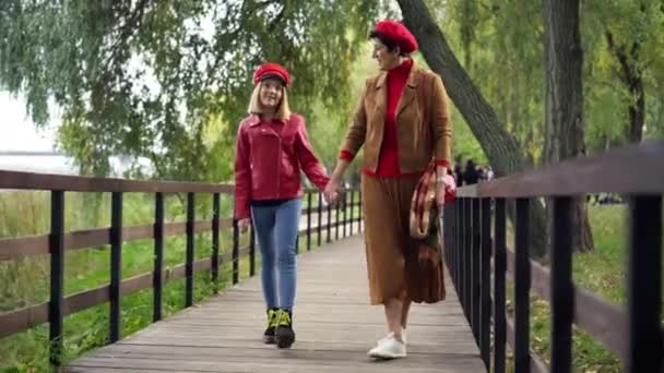 ワイドショットフロントビュー幸せな美しいおばあちゃんと孫娘が屋外で抱き合って歩いています 秋の公園でレジャーを楽しんでいる白人シニア女性と10代の少女の肖像画 — ストック動画