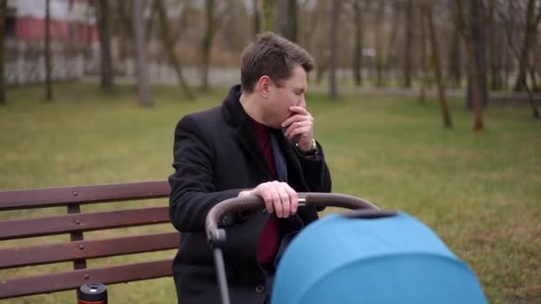 유모차를 공원에서 벤치에 스러운 신생아와 불편한 코카서스 아버지의 초상화 — 비디오