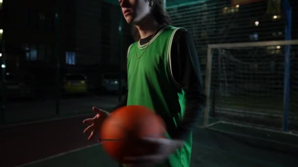 認識できないフィット感の若いスポーツマンは 屋外の夜の暗闇に立っているバスケットボールボールをジャグリング 市街地で競技スポーツトレーニングをする白人男性 — ストック動画