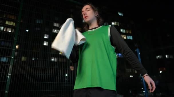迷惑疲惫的运动员扔掉篮球 擦去脸上的汗珠 然后走开了 一个疲惫的白人年轻人夜间在城市室外训练的画像 — 图库视频影像