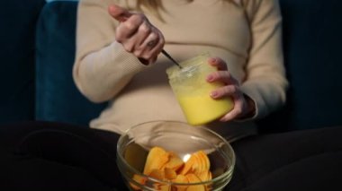 Ön manzara tanınmayan hamile, beyaz bir kadın içeride oturmuş bal ve patates cipsi yiyor. Tatlı ve tuzlu fast food 'la bekle.