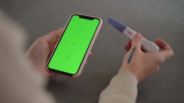 高视角的绿色屏幕智能手机和白人女性手中的阳性妊娠测试 室内电话申请模板的特写镜头 无法辨认的年轻孕妇 — 图库视频影像