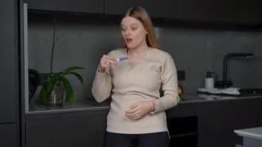 Heyecanlı mutlu kadın portresi pozitif hamilelik testi dansı ile evde mutlu bir şekilde. Neşeli, neşeli, beyaz, gülümseyen, içeride iyi haberler alan biri.