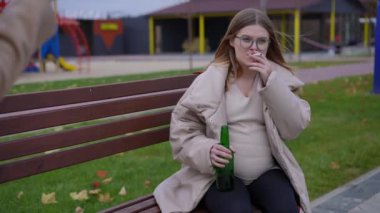 Bira şişesi ve sigarayla bankta oturan hamile bir kadının portresi. Beklenmedik bir şekilde yaklaşan tanınmaz bir kadın. Beyaz kadın jest yapan kadını dinliyor.