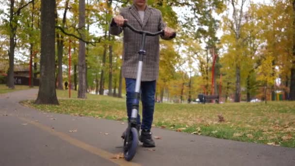 无法辨认的白人男孩骑着踢踏车在公园小巷里缓缓离去 放松快乐的孩子在户外享受秋天的周末 — 图库视频影像