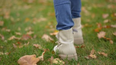 Sonbahar parkı çimlerinde tanınmayan küçük bir kızın yavaş çekim adımları. Kapalı hava gününde çayırda gezinen çocuğun yakın çekim görüntüsü.