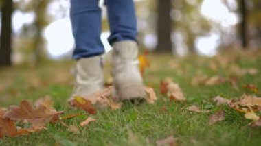 Canlı kamera, Meadow 'daki sonbahar parkında ağır çekimde yürüyen, beyaz çizmeli, tanınmayan kızı takip ediyor. Arka plan görüntüsü, düşen yapraklarla yeşil çimlerde gezinen çocuk görüntüsü.
