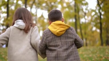 Yavaş çekimde yokuş yukarı koşan mutlu çocuk ve kızın izini sürüyorum. Orta boy beyaz arkadaşlar güz gününde dışarıda eğlenirken çekiliyor.