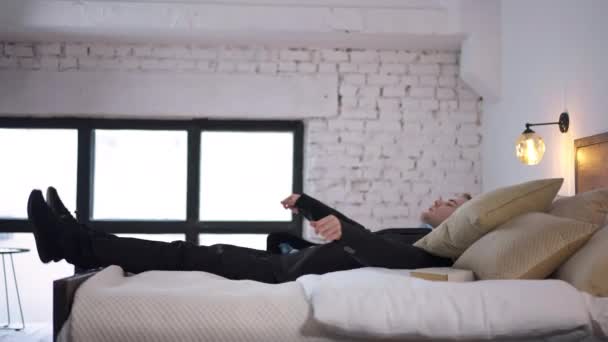 サイドビュー スーツの幸せな疲れた男は ゆっくりとした動きでベッドに落ちて跳び上がります ワイドショット 満足するコーカサスフリーランスのビジネスマン屋内自宅の寝室で — ストック動画