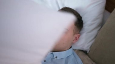 Esmer, beyaz, yorganı yavaş çekimde kaldıran genç bir adam gömlekle yatakta yatıyor. Kendine güvenen bir iş adamının yatak odasında kestirirken yüksek açılı portresi.