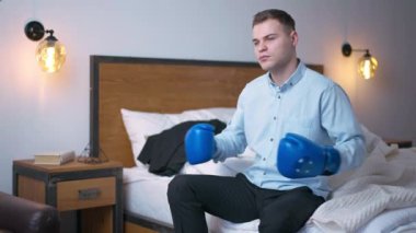 Kendine güvenen genç işadamının orta boy portresi ağır çekimde boks eldivenlerine vuruyor. Kafkasyalı bir adam yatağında otururken kafasını çeviriyor.