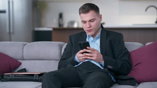 Takım Elbiseli Genç Adam Kanepeye Oturmuş Akıllı Telefon Dokunmatik Ekranında — Stok video