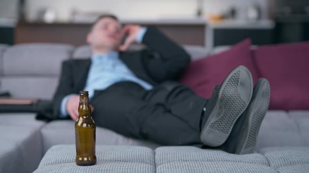 Butelka Piwie Męskie Stopy Butach Kanapie Zamazanym Biznesmenem Rozmawiającym Przez — Wideo stockowe