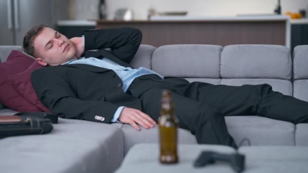 疲れ果てた若者の肖像画は 前面にぼやけたビール瓶とゲームコントローラーとソファーに適しています 疲れたコーカサスフリーランサー 金曜日リビングルームの自宅で — ストック動画