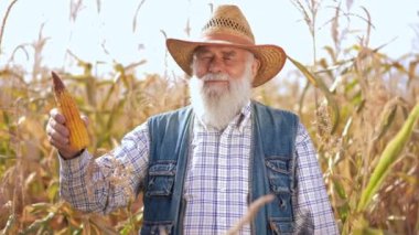 Olgun mısırla tatmin olmuş çiftçinin portresi yavaş çekimde gülümseyen kameraya bakıyor. Orta ölçekli, mutlu, kendine güveni tam, dışarıda poz veren beyaz bir adam.