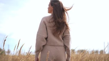 Buğday tarlasında duran kendine güvenen bir kadın yavaş çekimde sapına dokunur. Kafkasyalı yetişkin kadın bulutlu bir sonbahar gününün tadını çıkarıyor.