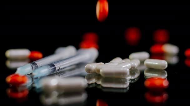 白い薬と注射器でテーブルの上に落ちる赤い丸薬を閉じる ブラックバックでのクローズアップ薬 — ストック動画