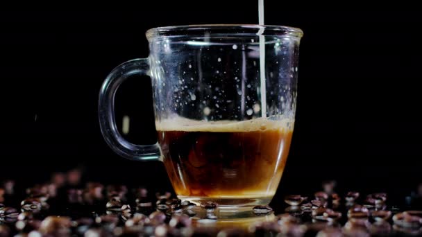 特写黑咖啡在透明的杯子里 白牛奶慢动作地倒入 将香喷喷的热饮料与豆子一起放在桌上 — 图库视频影像