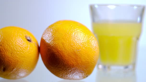 オレンジからオレンジジュースに焦点を当て ホワイトバックグラウンドでテーブルの上にグラスに クローズアップおいしいおいしいオーガニックビタミンフルーツと飲料 — ストック動画